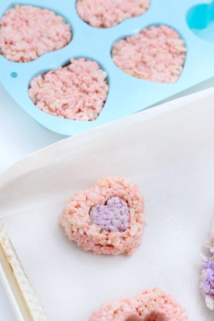 We made some festive Valentine's Day Rice Krispies Treats & you gotta make them this Valentine's Day! Perfect for school treats, office or your Valentine! #ValentinesDay #RiceKrispiesTreats #CerealTreats Purple rice treat heart is placed inside pink heart rice treat and placed on tray.