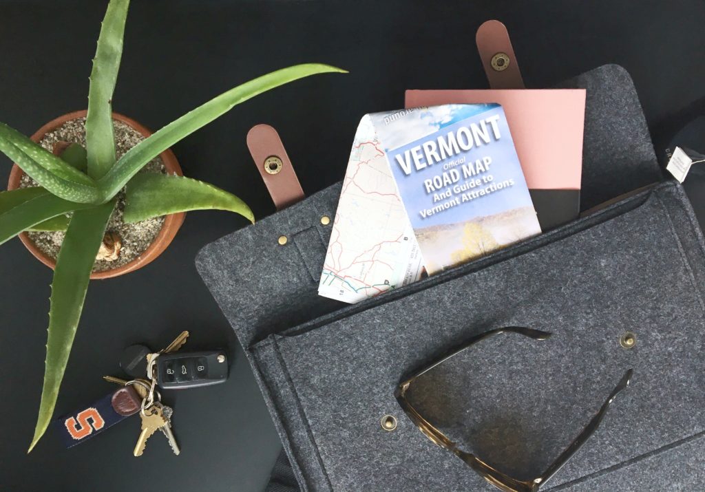 Messenger bag with Vermont road map, flat lay with keys, plant, and sunglasses. 