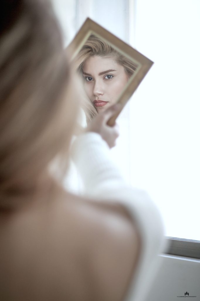 A pretty woman looks at herself in a small square mirror turned sideways.