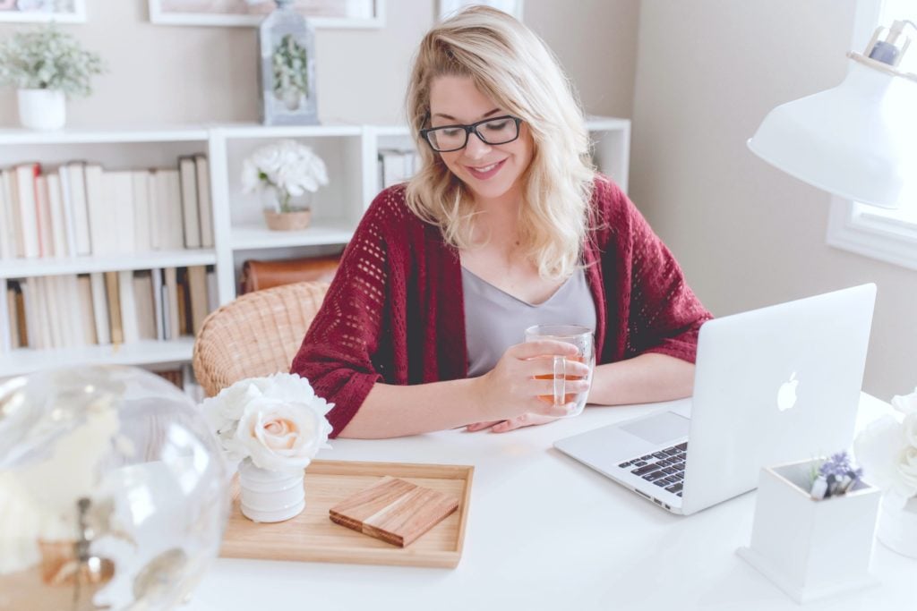 A woman smiles while workinh on her Macbook.