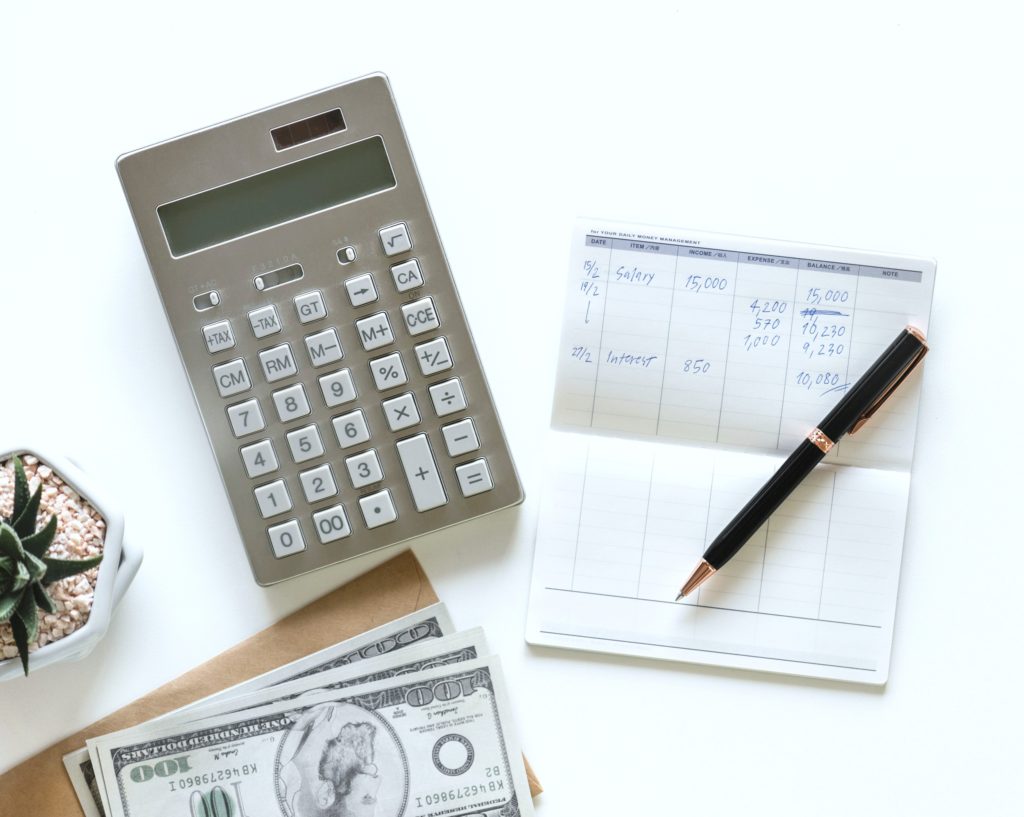 Flat lay of calculator, budget book, pen, money, and succulent plant. 