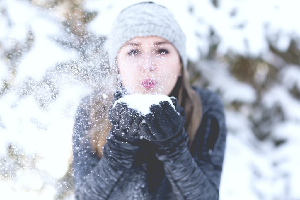 Girl blows a handful of snow from hands and towards the camera.