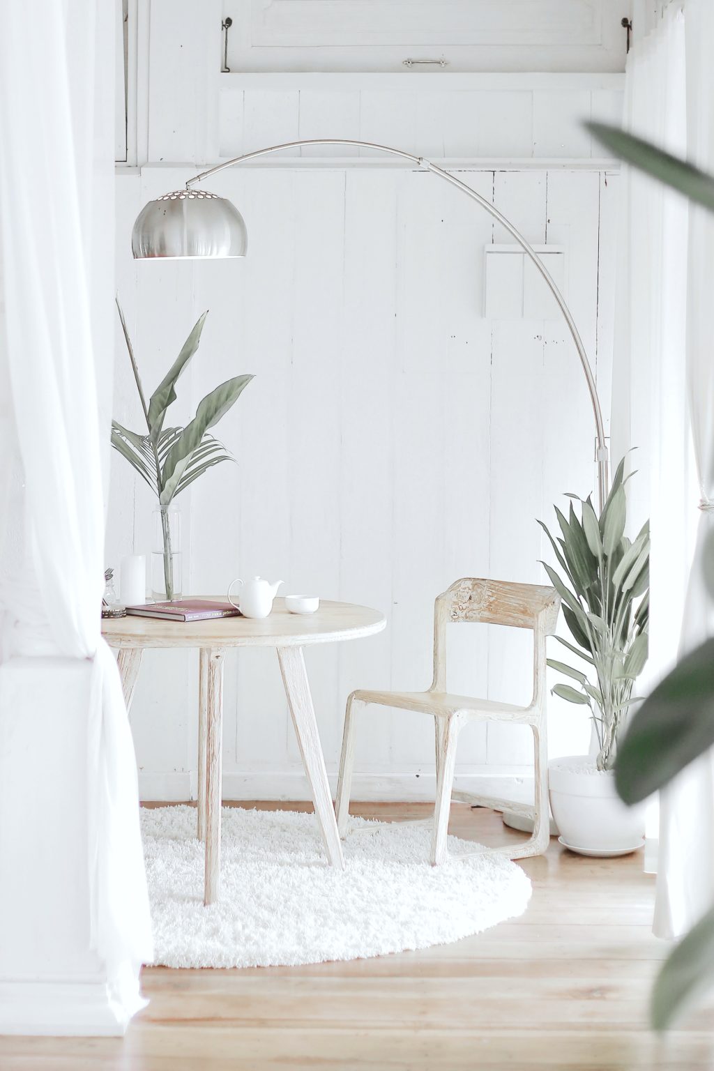 Neutral living space with green plants, neutral wood table and chair and silver lamp.