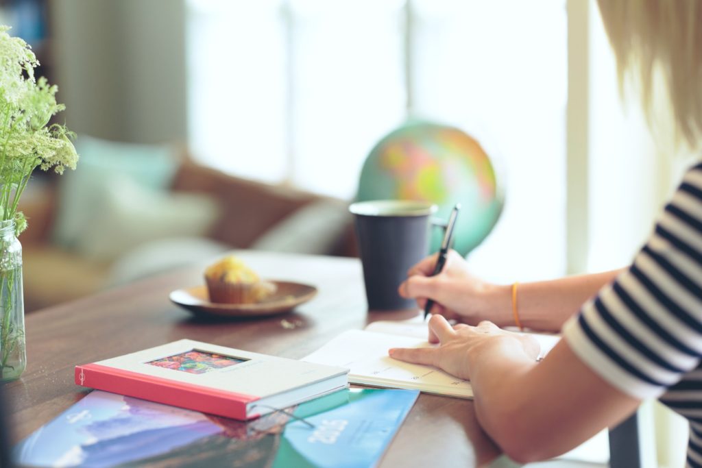 Student sitting at desk doing homework and writing in a notebook. 