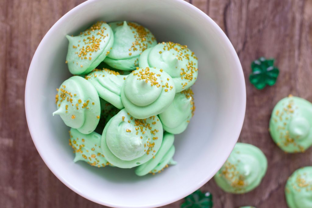 A white bowl with about 12 green meringue drops that look like medallions, sprinkled with golden sprinkles/flecks.