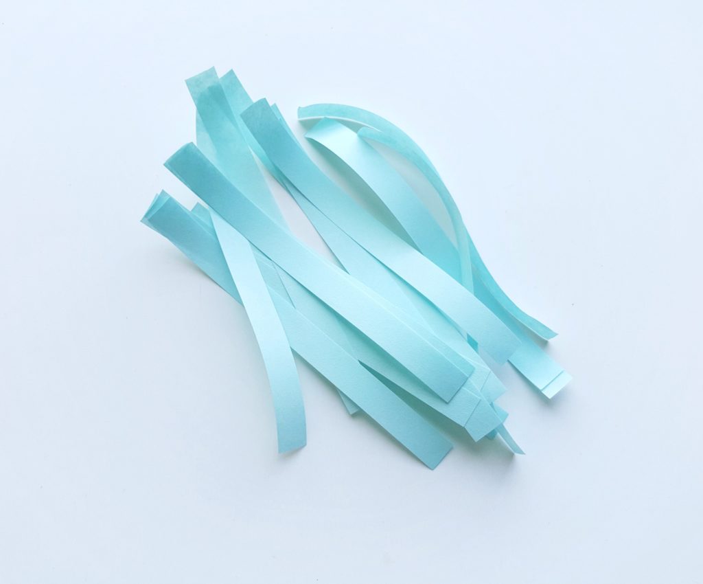 Light blue strips of paper, ready to be quilled. 