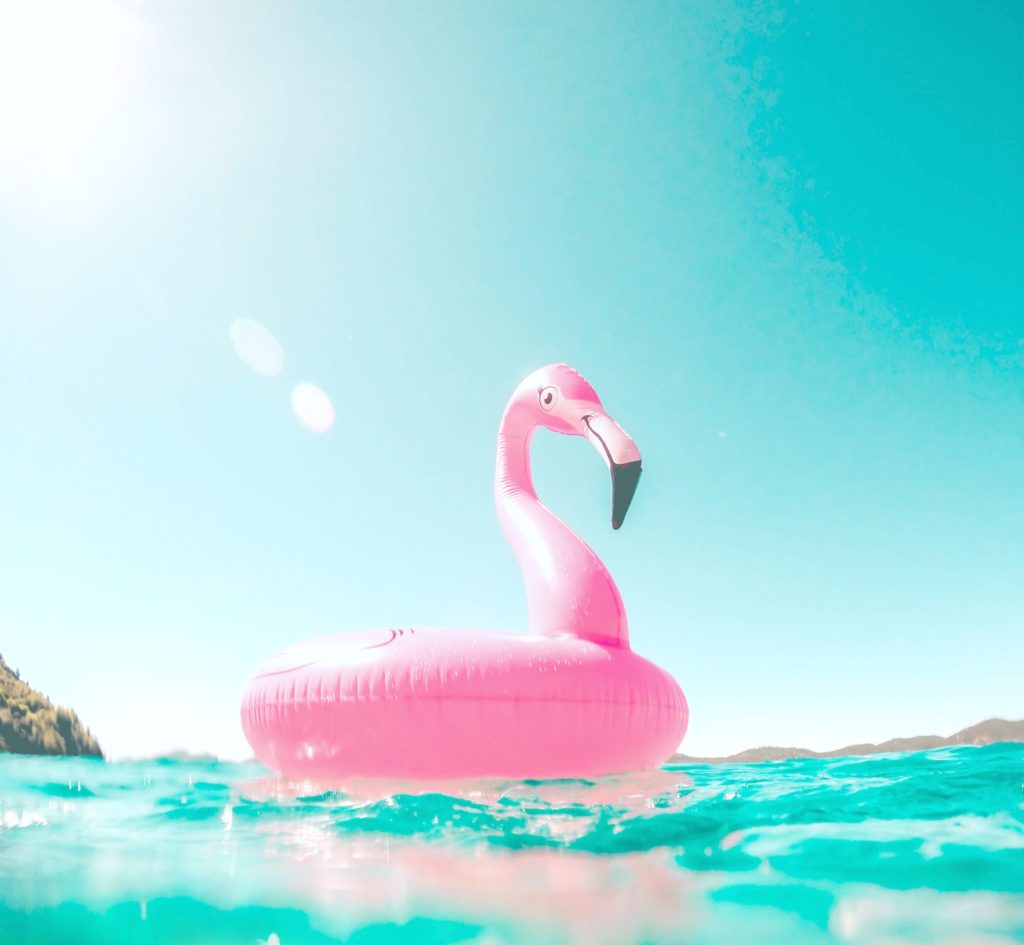 A pink flamingo pool float is floating in the sea, it is close to the camera in the water.