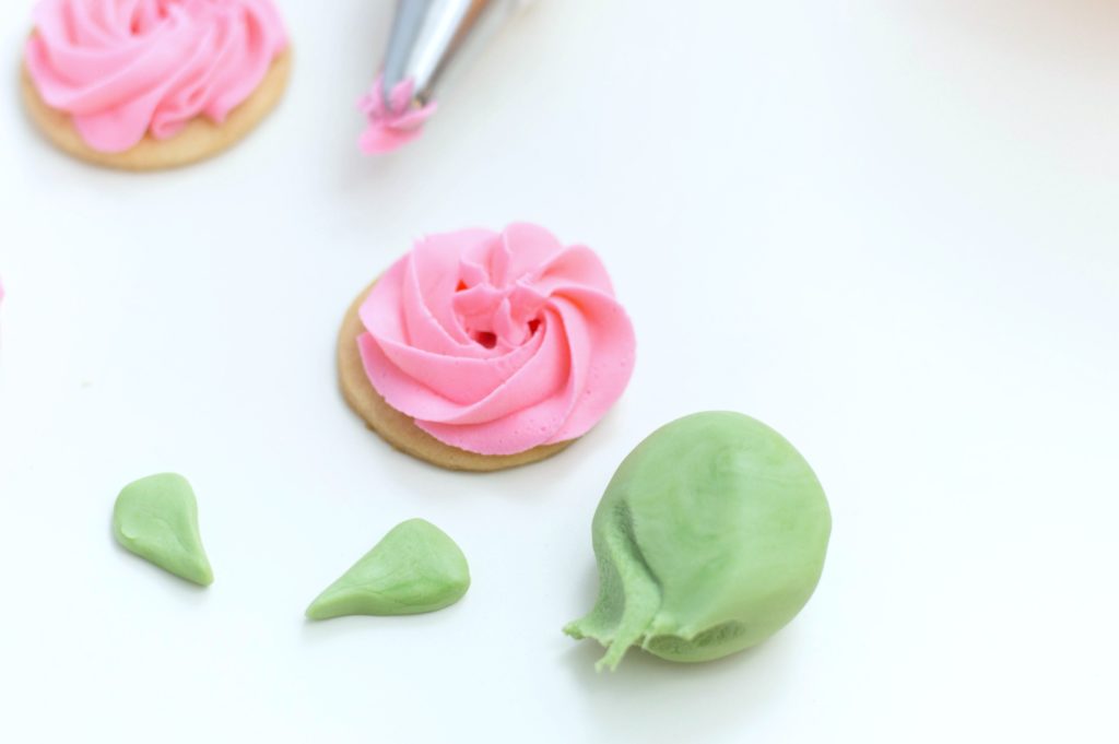 Two frosted cookies with a ball of green fondant that is being formed into leaves.