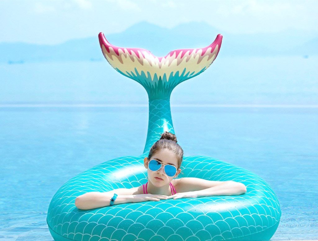 A girl floats inside a mermaid float, the tail makes it look like it is the girl's tail. 