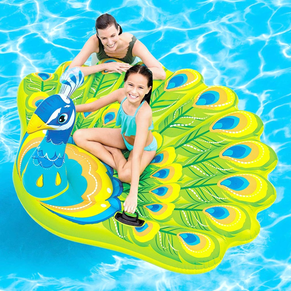 A woman and a girl float in a pool on top of a peacock pool float. 