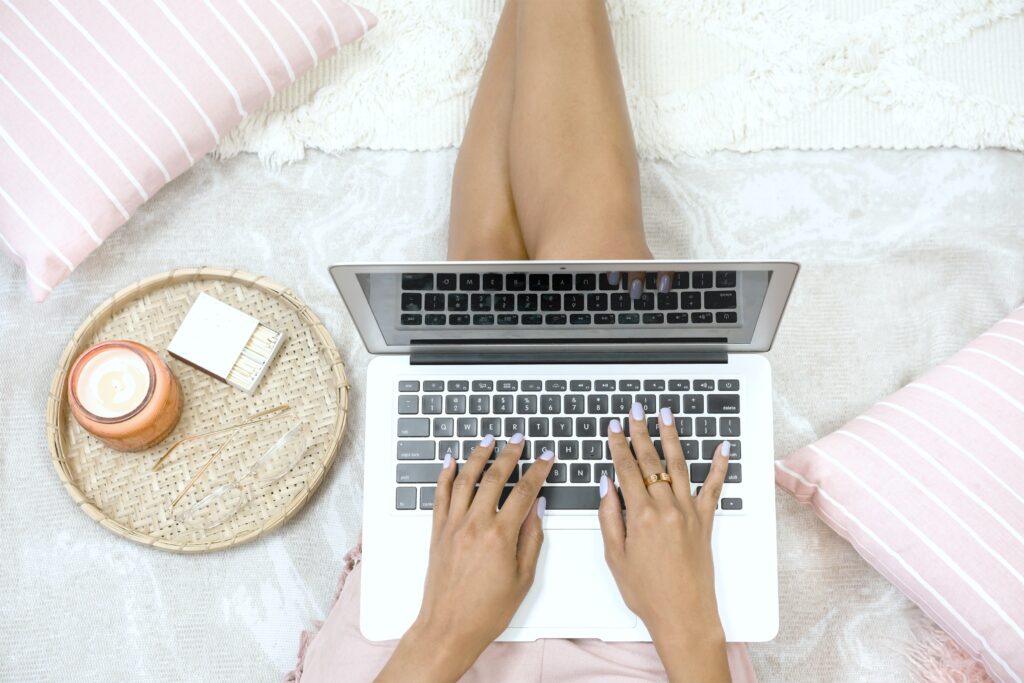 Woman in bed with laptop against a white and pink bed set.