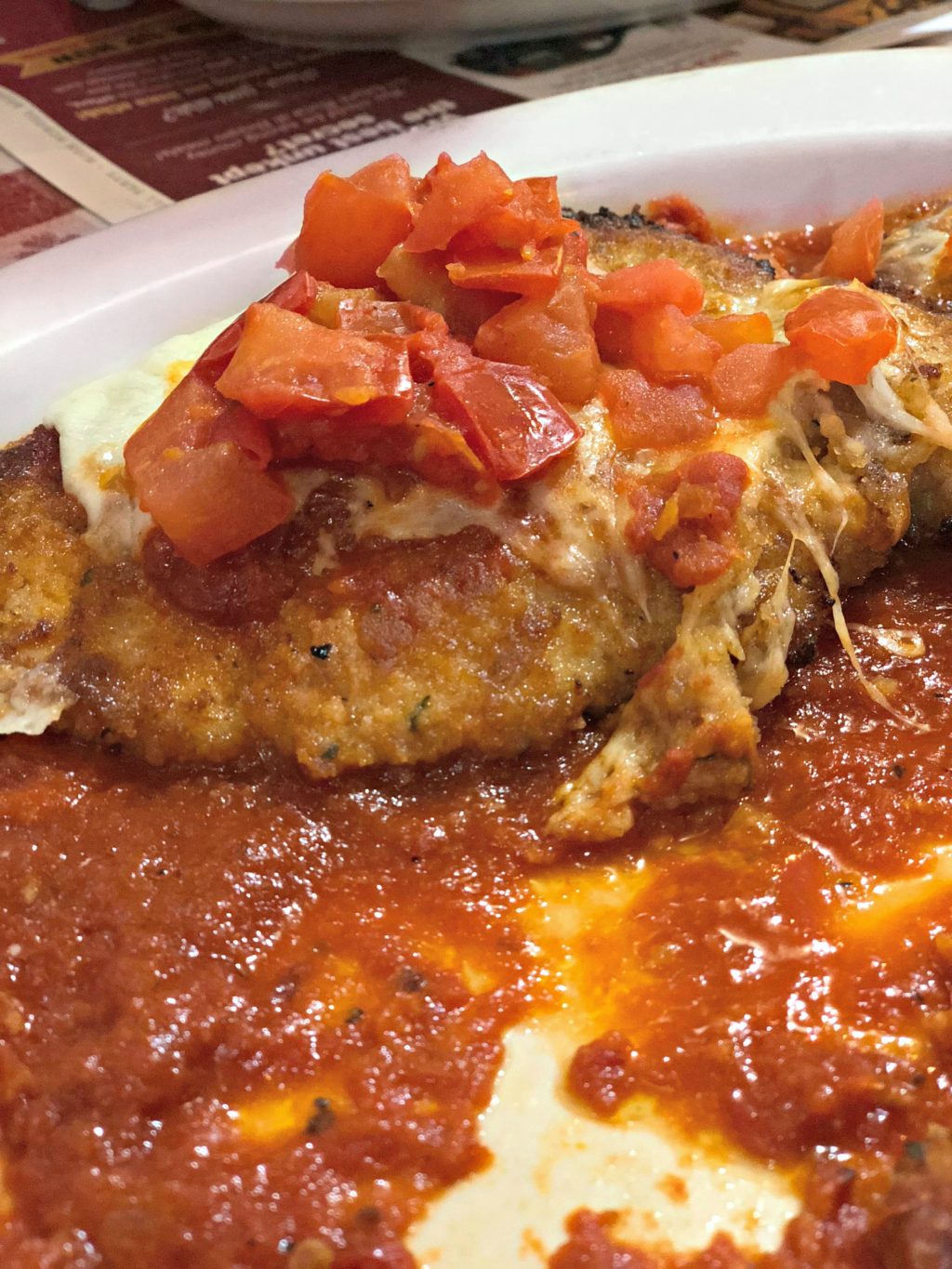 A perfectly breaded chicken breast sits atop fresh marinara, topped with fresh diced potato and melted cheese. 