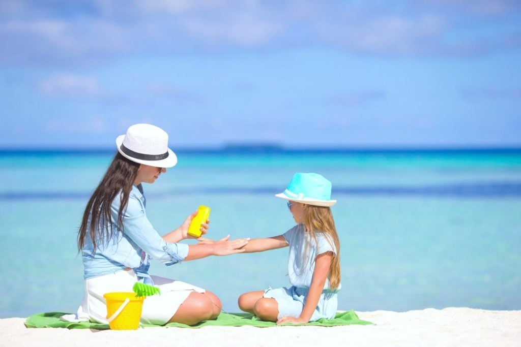 Mother putting sun screen on their child at the beach.