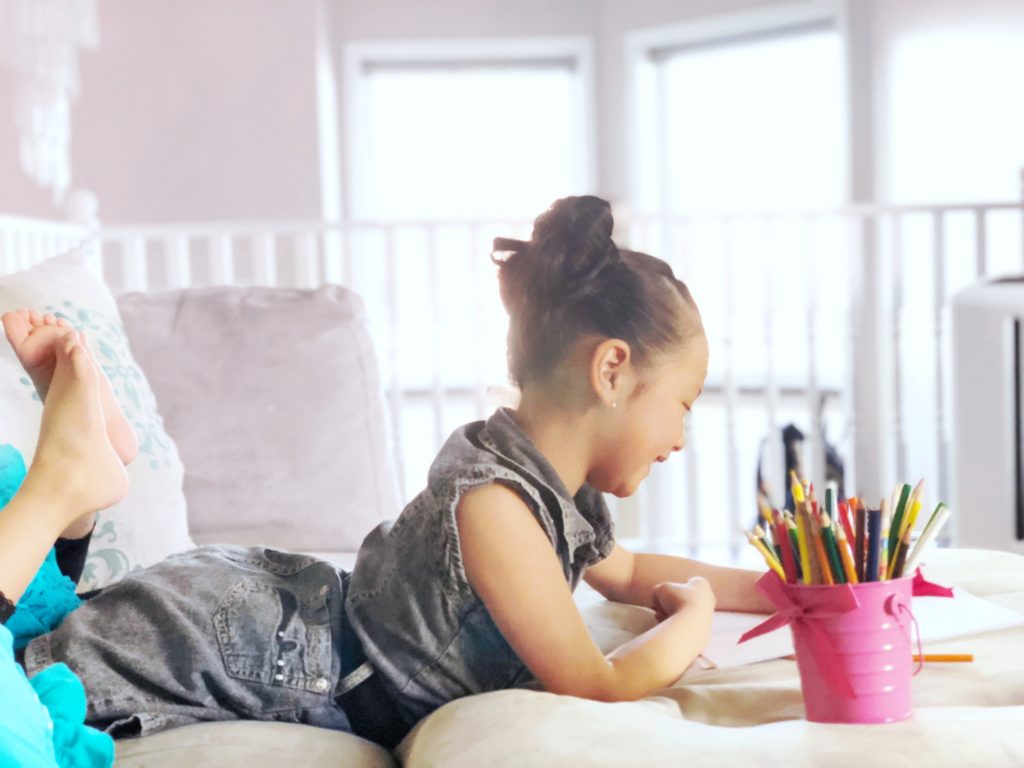 Little girl writes and draws happily while laying on couch.