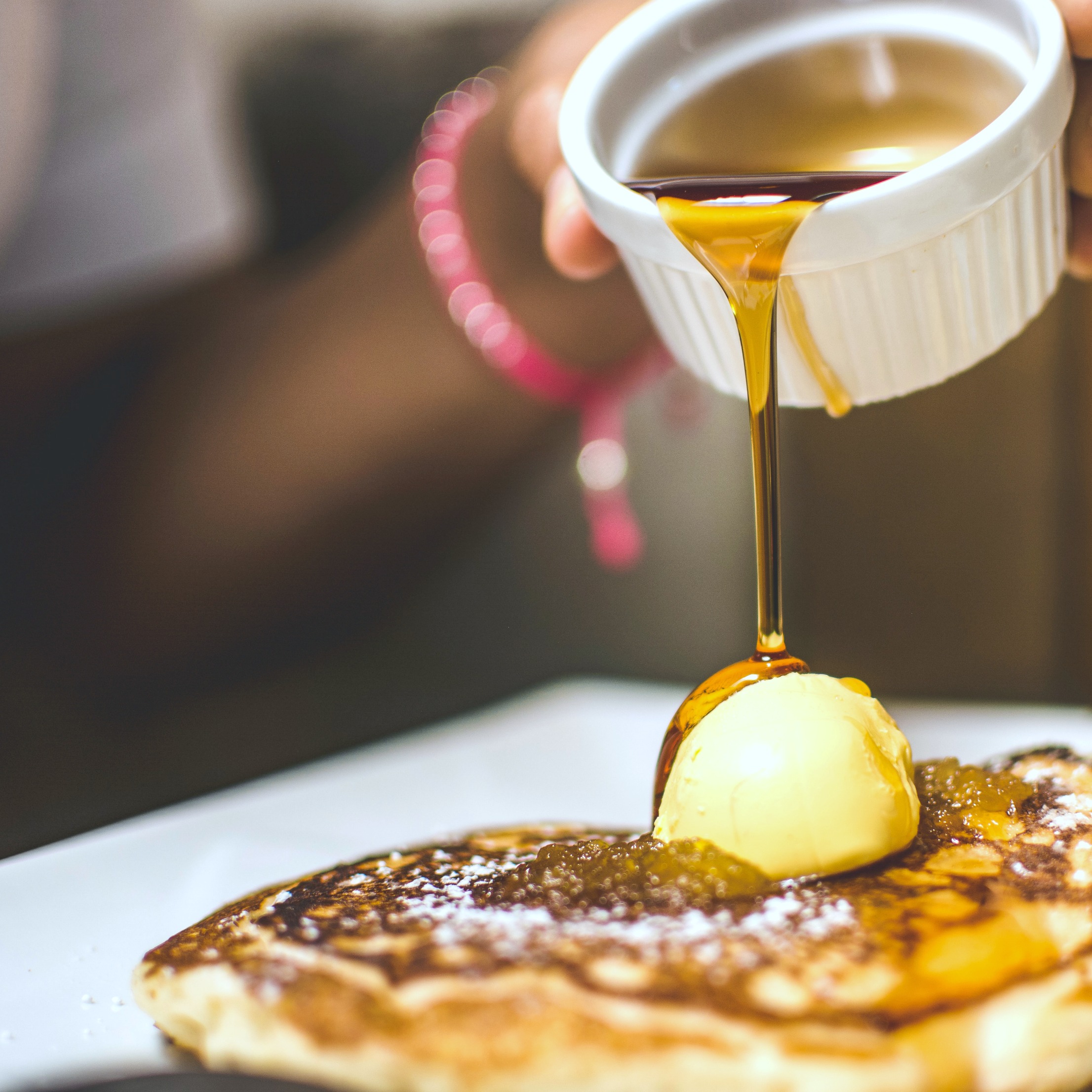 Someone pours syrup on top of traditional pancakes with butter. 