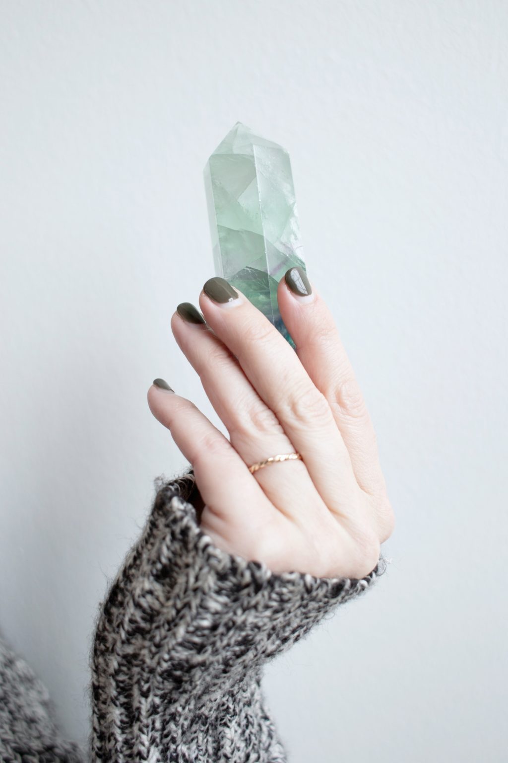 A woman wearing a grey wool sweater is holding a teal/aqua gemstone in her hand. 