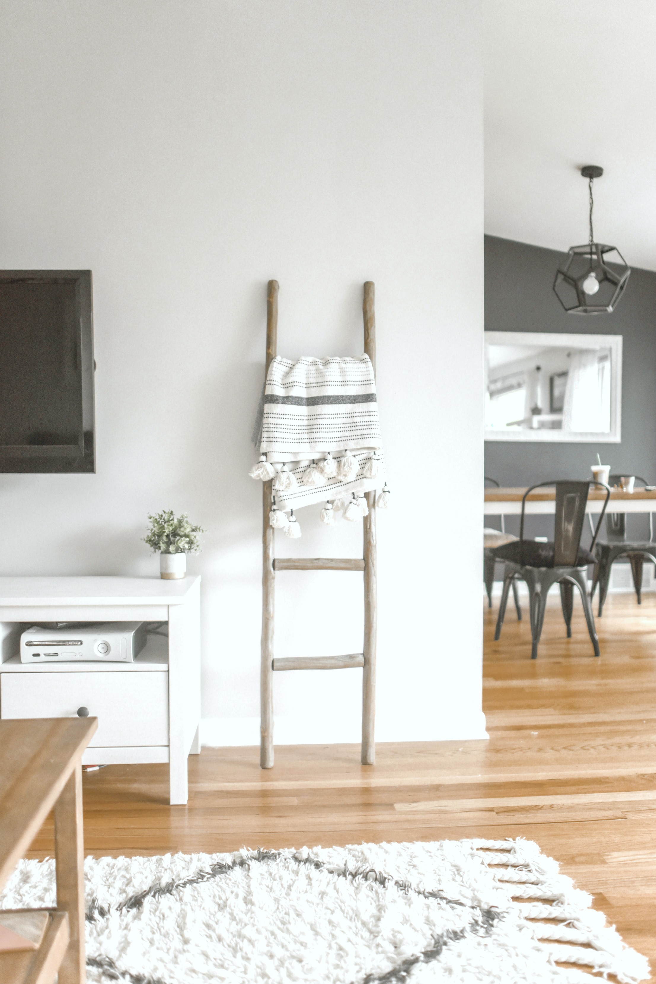 A beautiful home with textured rug, ladder holding throw pillows, with dining room pictured in the back. 