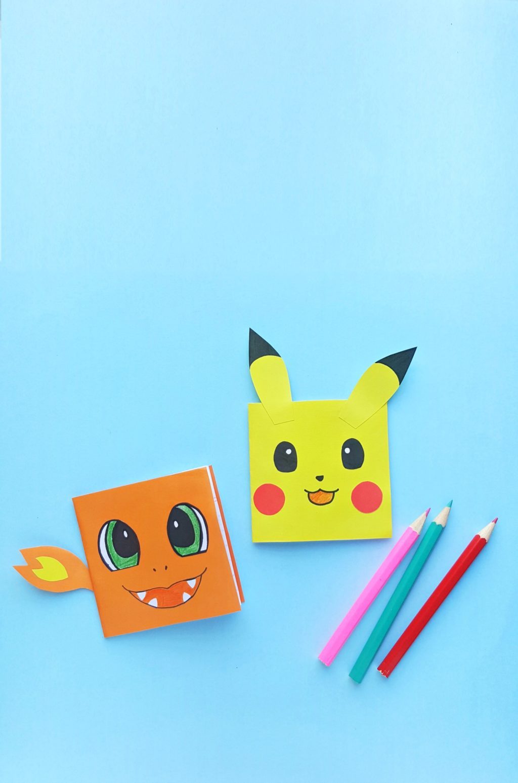 A blue background with DIY Charmander and Pikachu Notebooks with 3 pencil crayons.