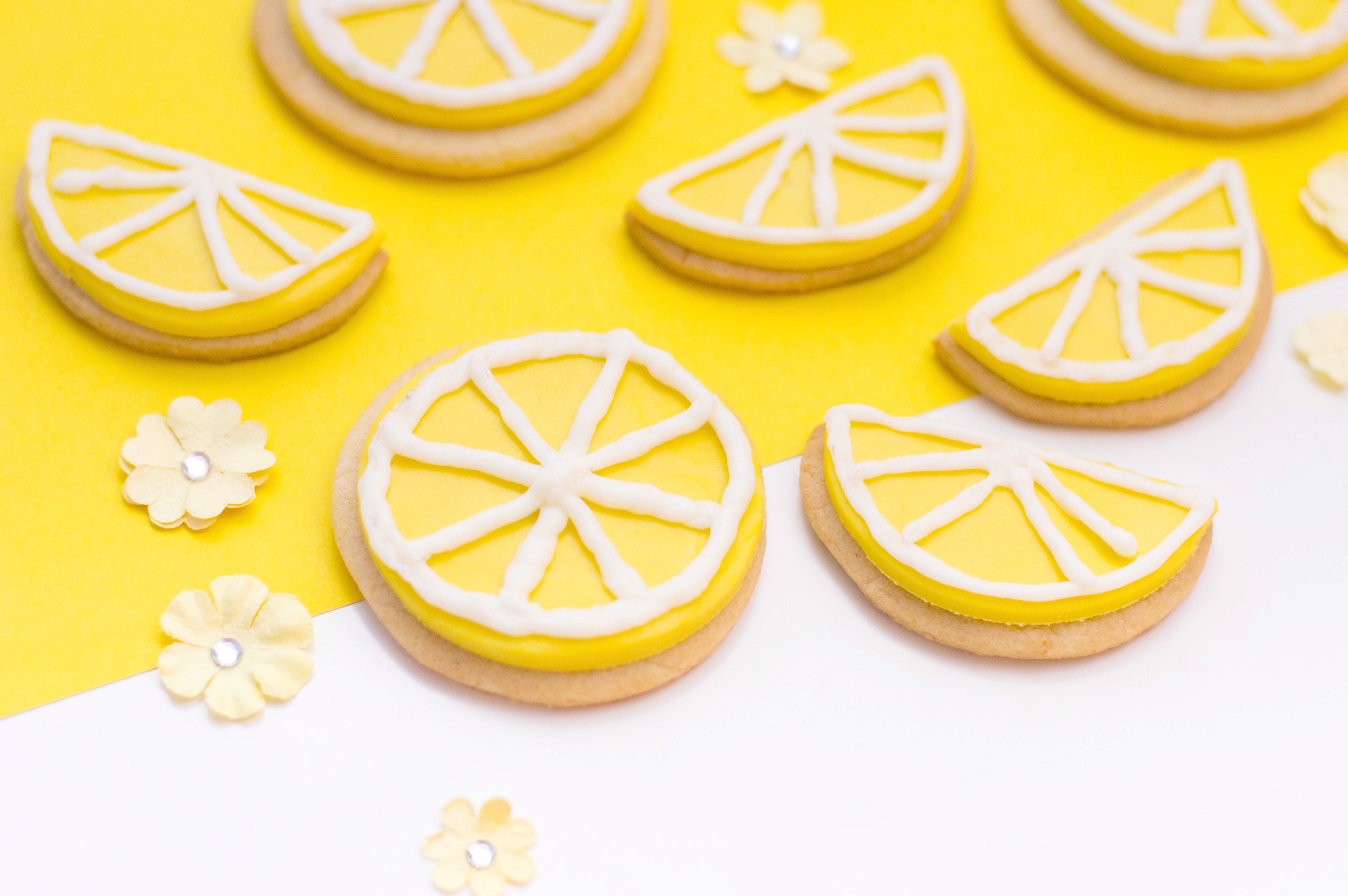 Close up of lemon slices and wedges sugar cookies, iced and ready to eat on a yellow and white background. 