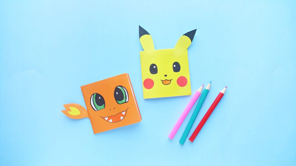 A blue background with DIY Charmander and Pikachu Notebooks with 3 pencil crayons.
