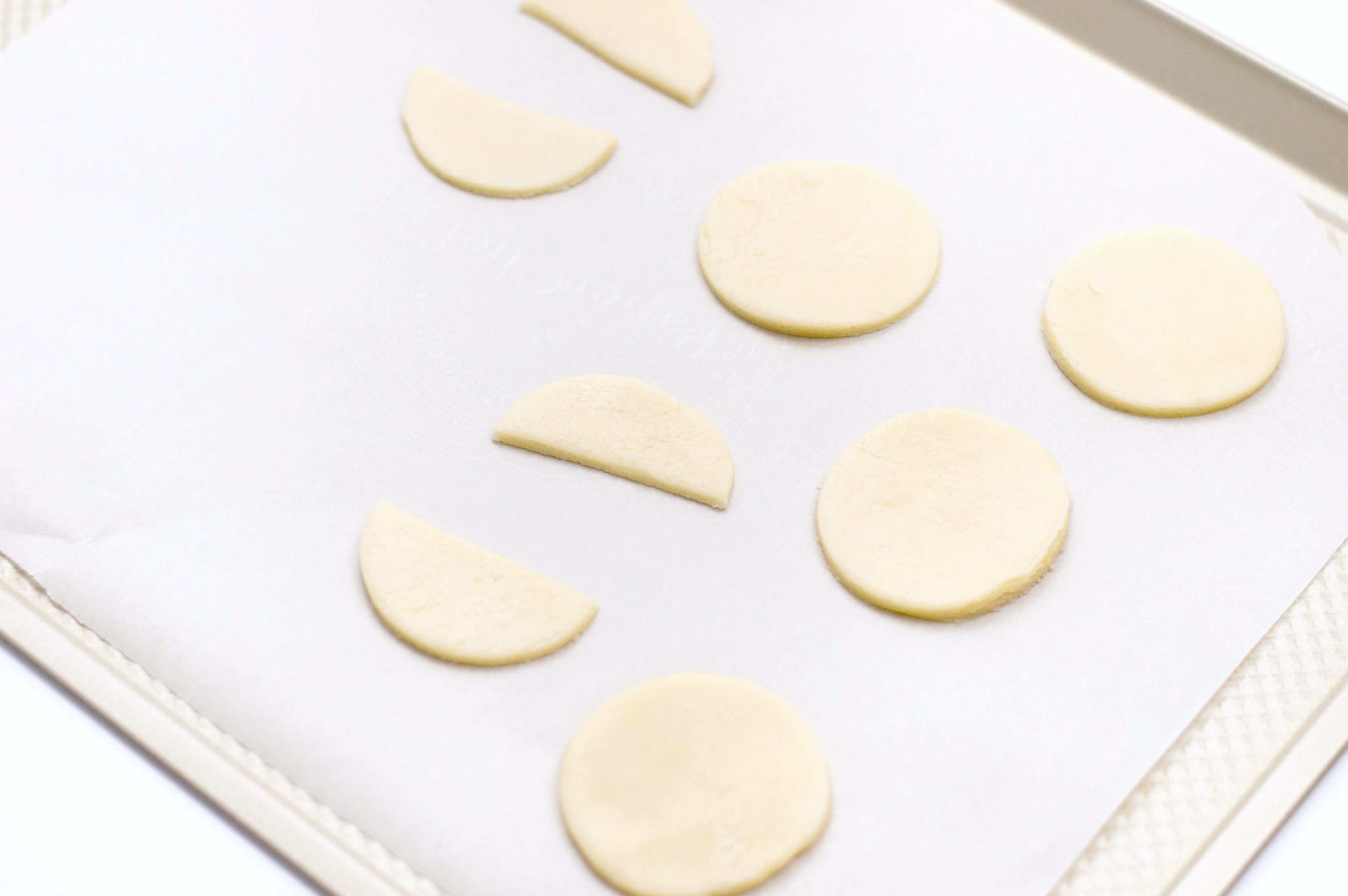 Cookies cut into circles and half circles and placed on a lined baked sheet. 