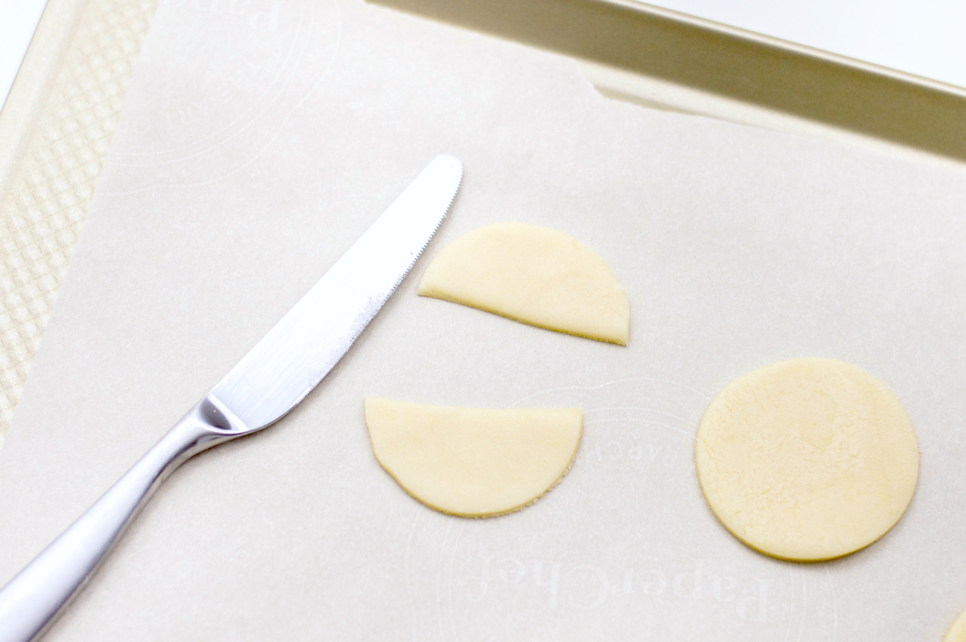 Sugar cookie circles being cut in half by butter knife. 