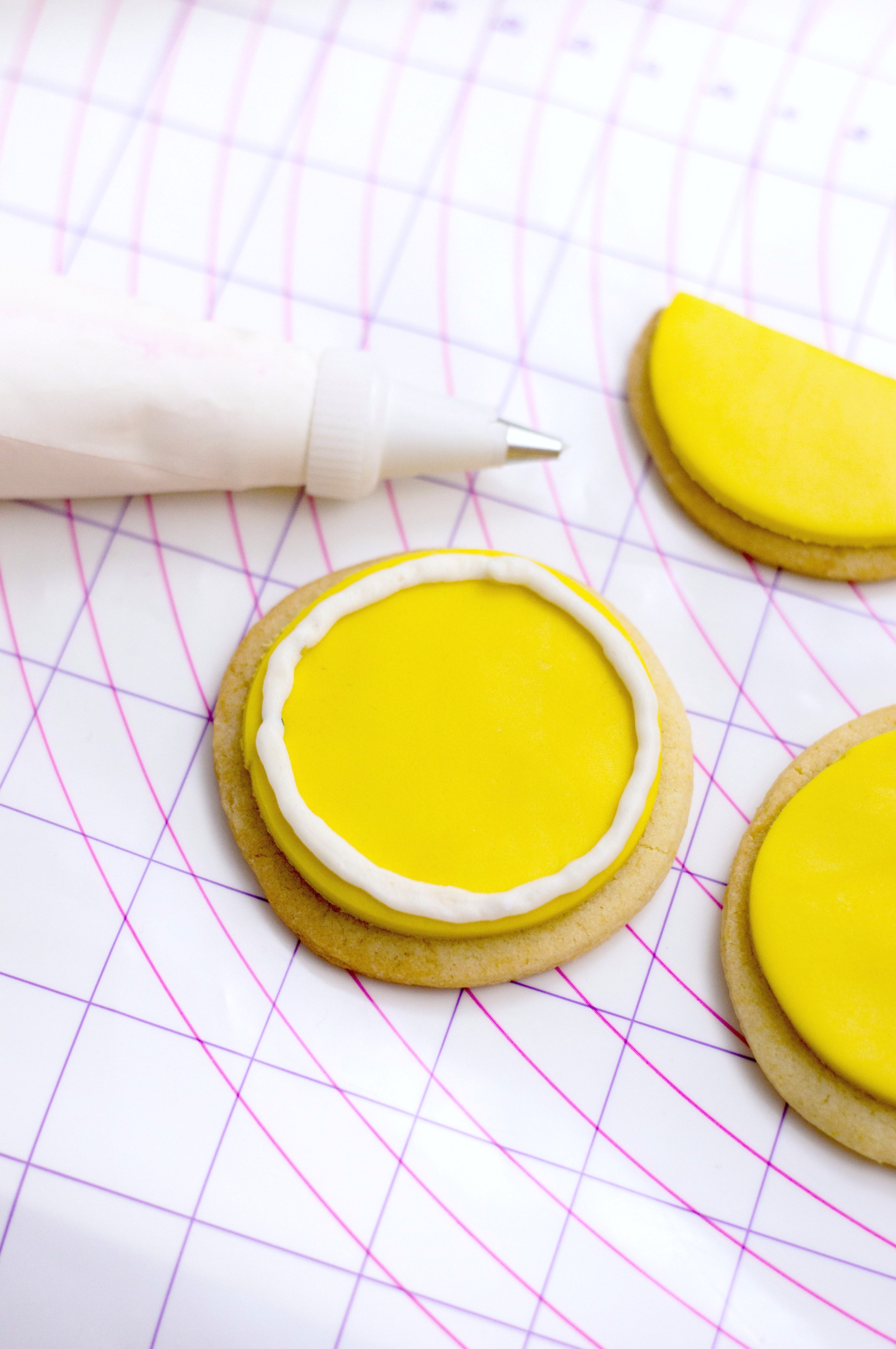 Cookie shown with fondant and a buttercream circle is traced around the yellow fondant circle. 