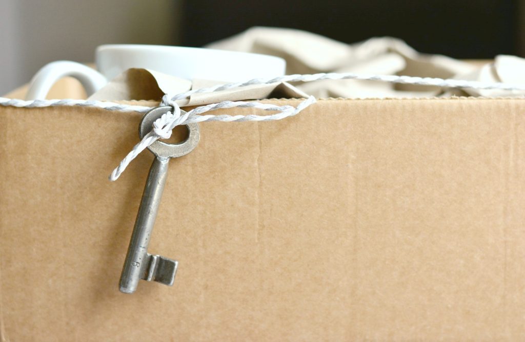 A box filled with mugs and a little key on a rope hangs off the mug and moving box. 