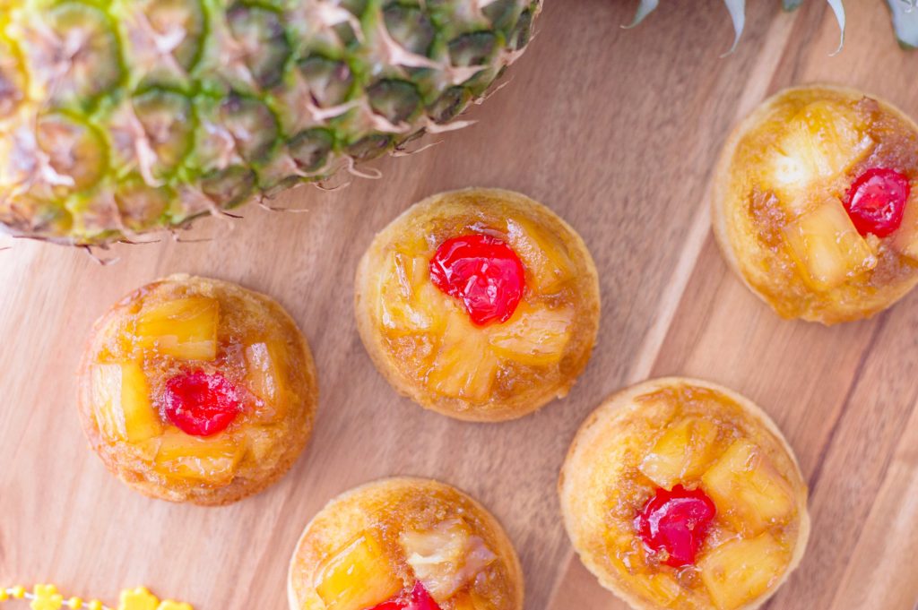 Top view of mini upside down pineapple cakes on a wood backdrop. Entire pineapple can be seen. 