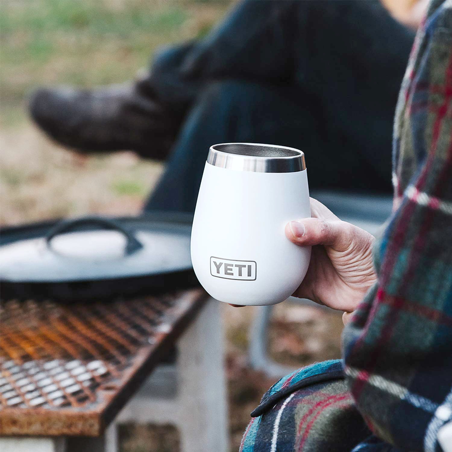 A woman holds a Yeti wine cup while wrapped a blanket around a fire. 