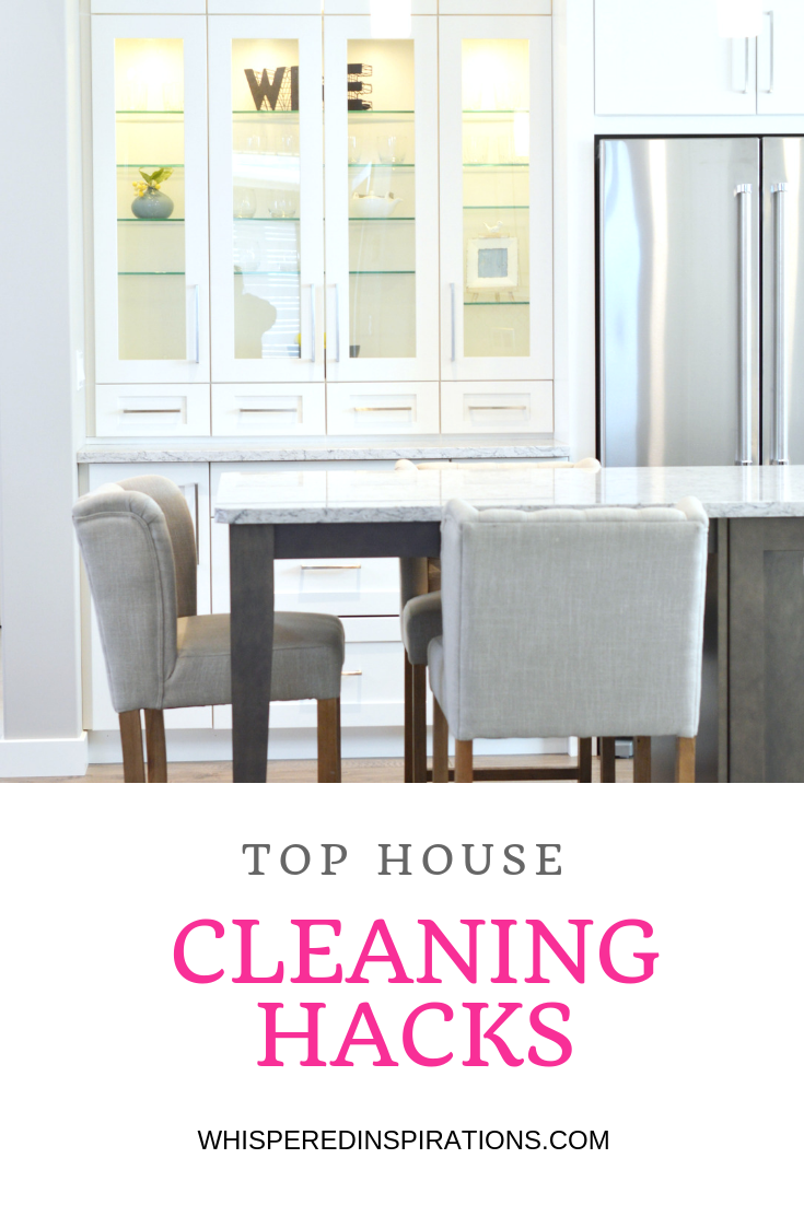 A beautiful white kitchen is shown, two chairs, an island, a stainless steel fridge and it's clean due to the top house cleaning hacks. 