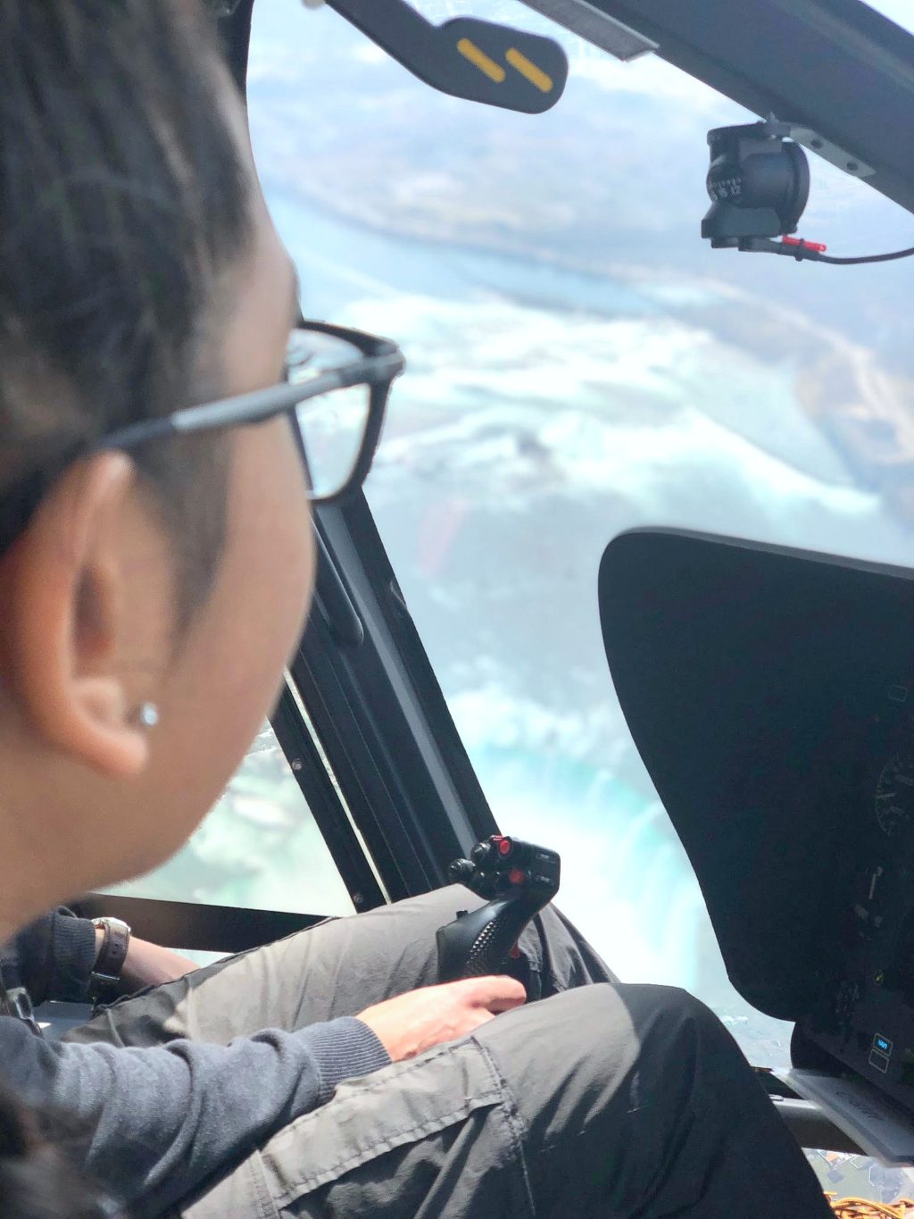 A girl looks out the window of a helicopter, while the pilot flies over Niagara Falls. 