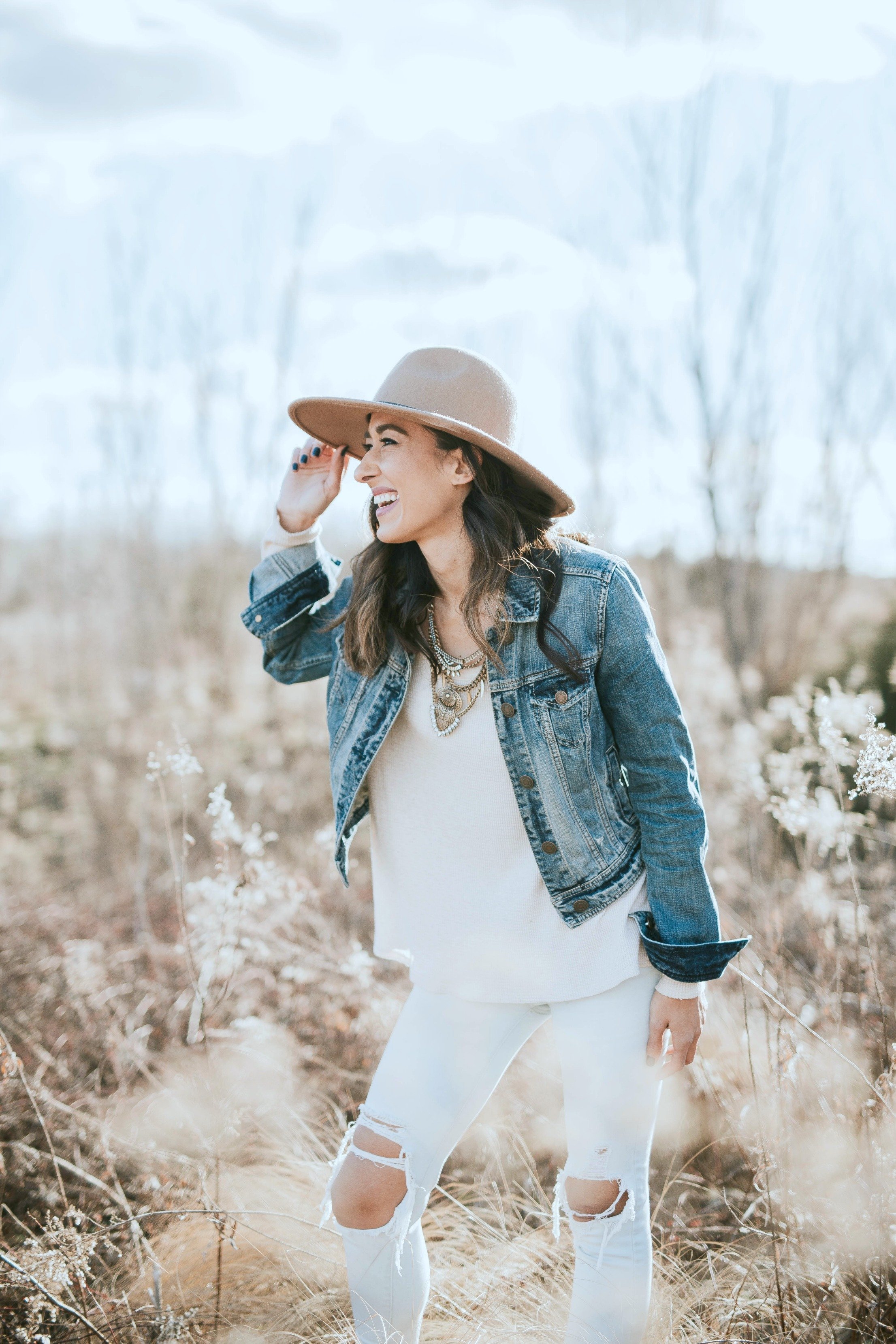 Woman smile in a field, she tips her hat and looks happy and confident. 