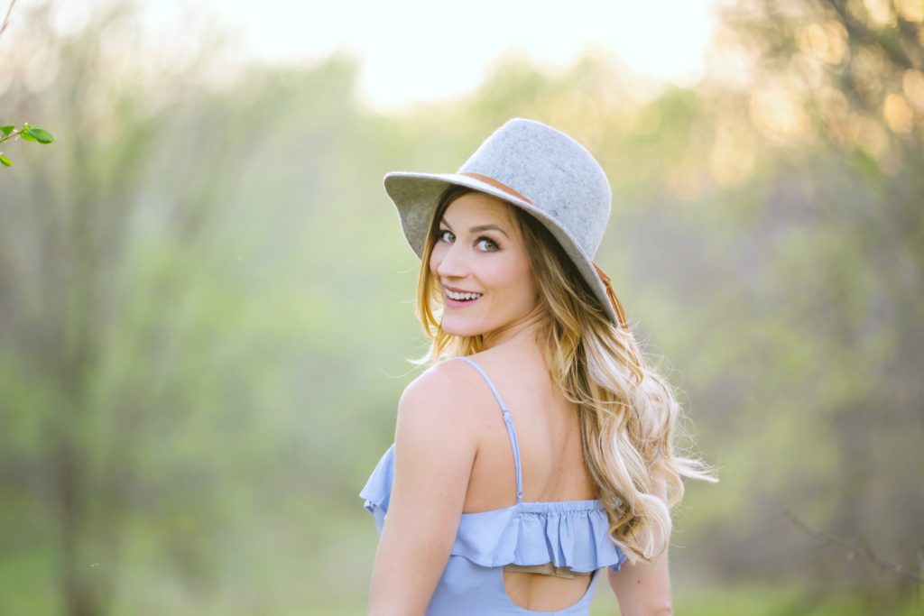 Woman wearing a grey hat looks back over her shoulder and smiles, the background is blurred and she is in focus. 