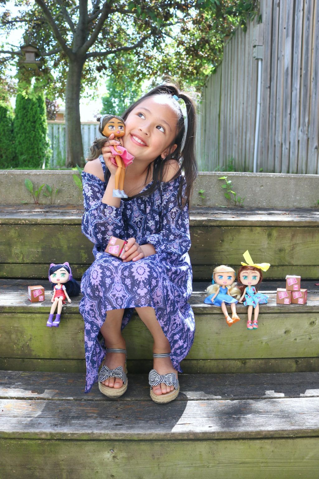 Mimi, a little girl, tilts her head and holds a Boxy Girl next to her cheek and smiles. 