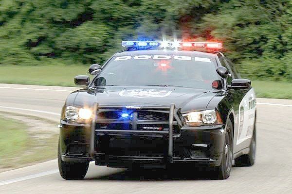 A Dodge Charger police squad car is racing down a track with all their lights on. 