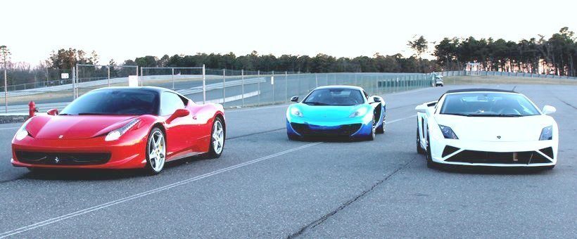 A Lamborghini, and two Ferraris are shown on a race track, waiting to be driven. 