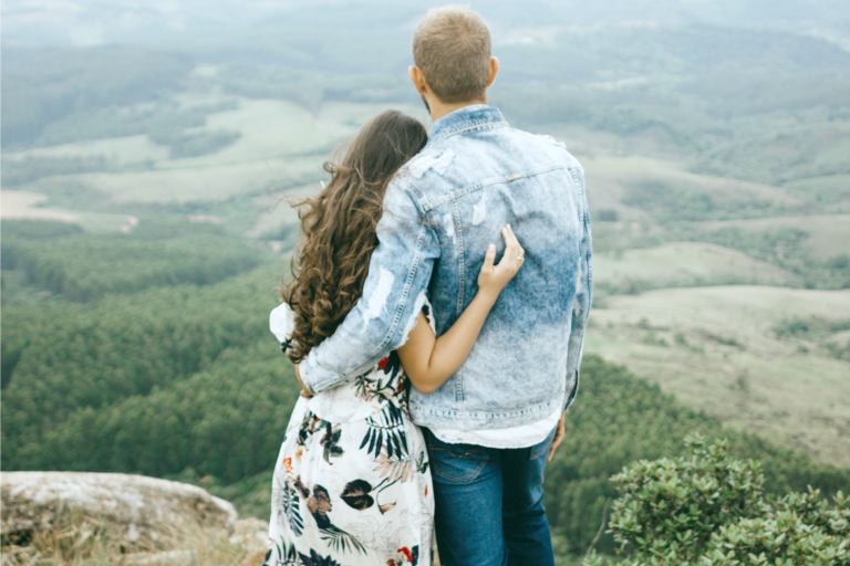 A young couple poses in front of a hillside facing towards the edge.
