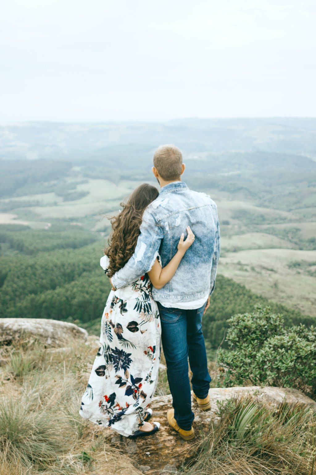 A couple looks over a hill together, only their backs are seen.