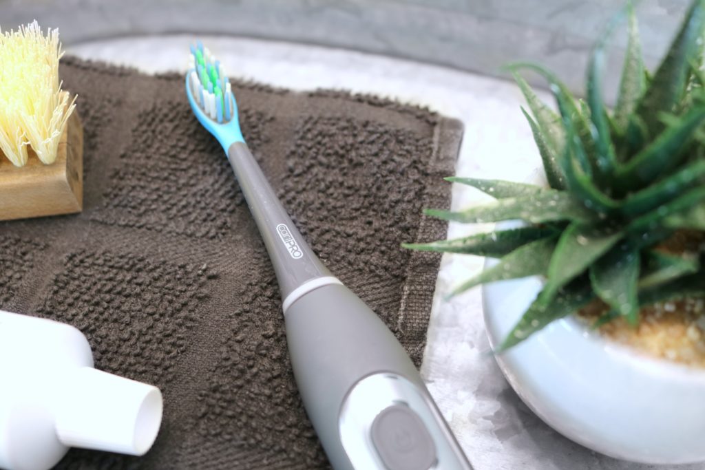 A close up of the cariPRO toothbrush. It rests on a towel, skin brush, and toothpaste. 