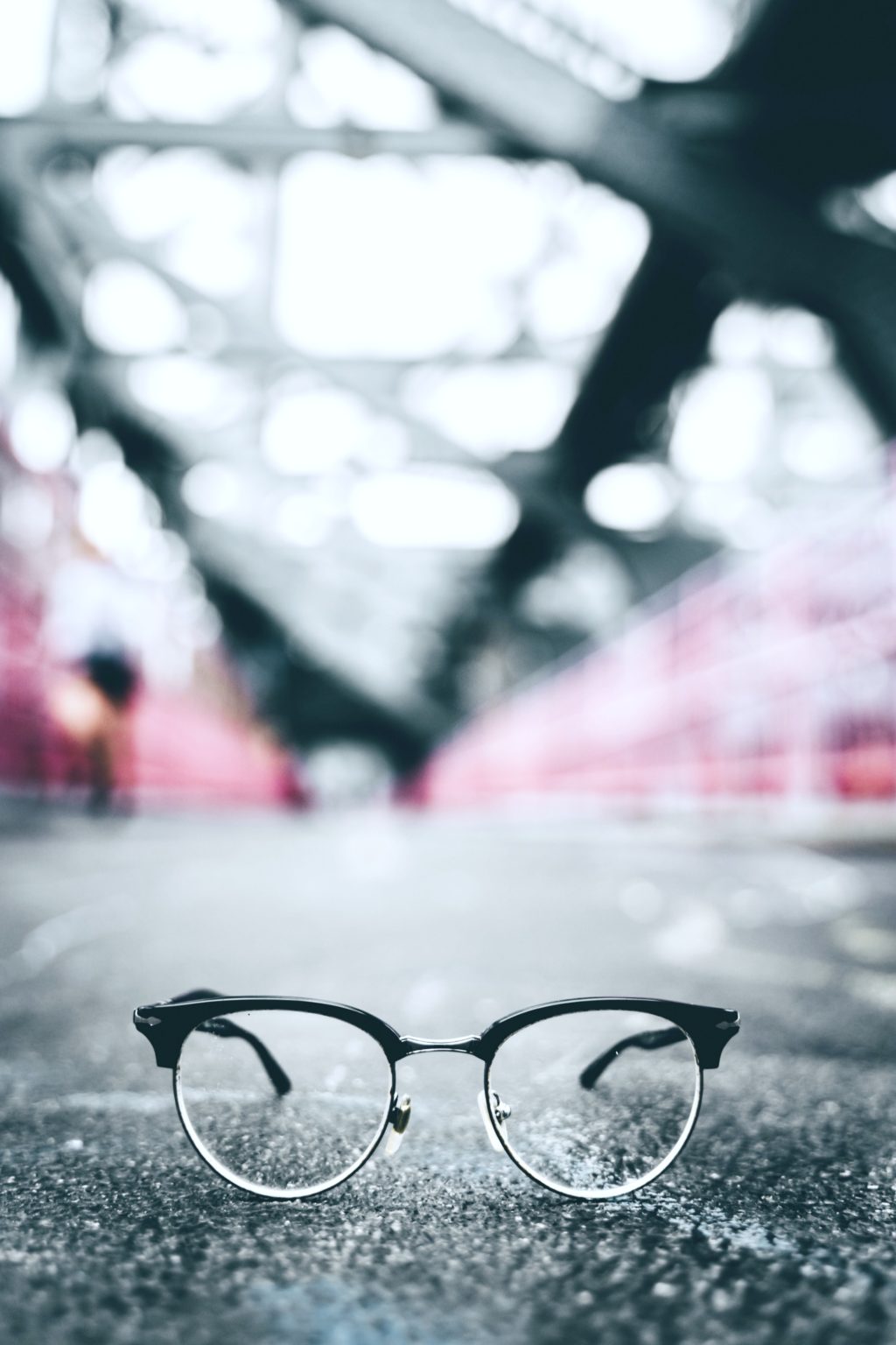 An artistic picture of Wayfarer glasses in an urban setting. They are on the concrete and looks like a blurred subway station in the back.