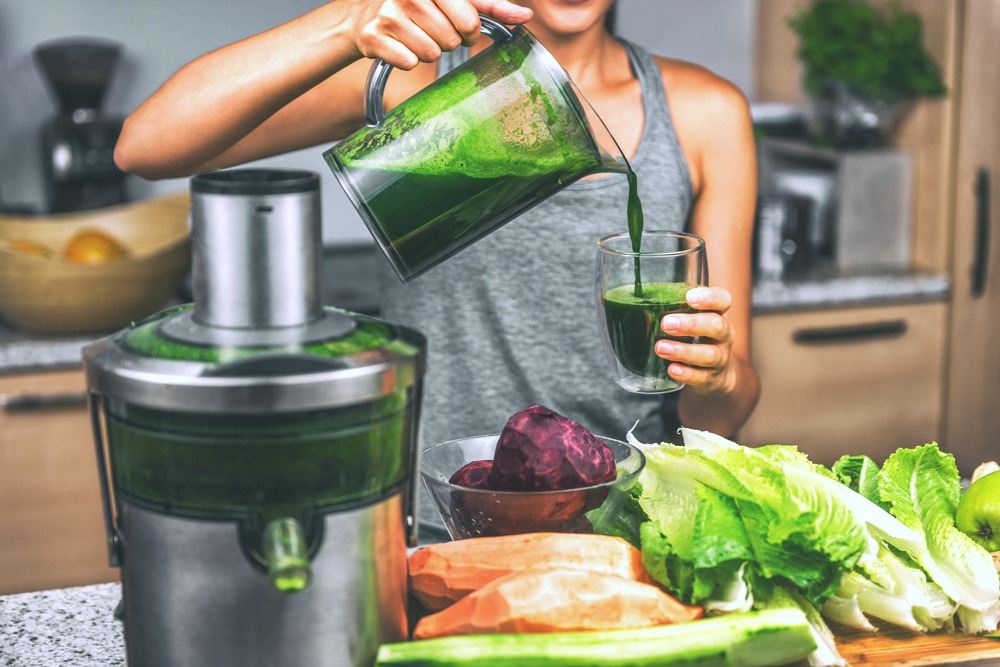 A woman juices veggies and makes green juice, she pours it into a cup. 