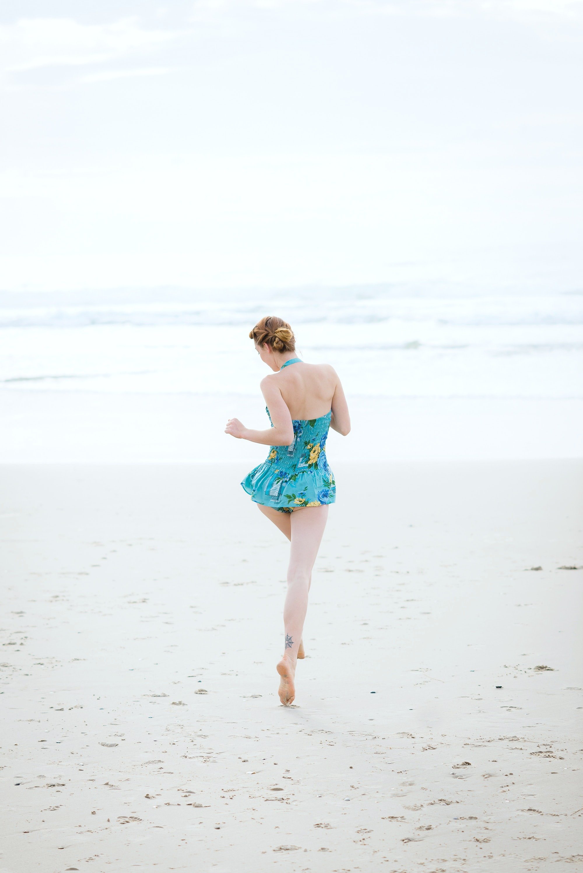 Woman prancing on the beach in a blue bathing suit. 