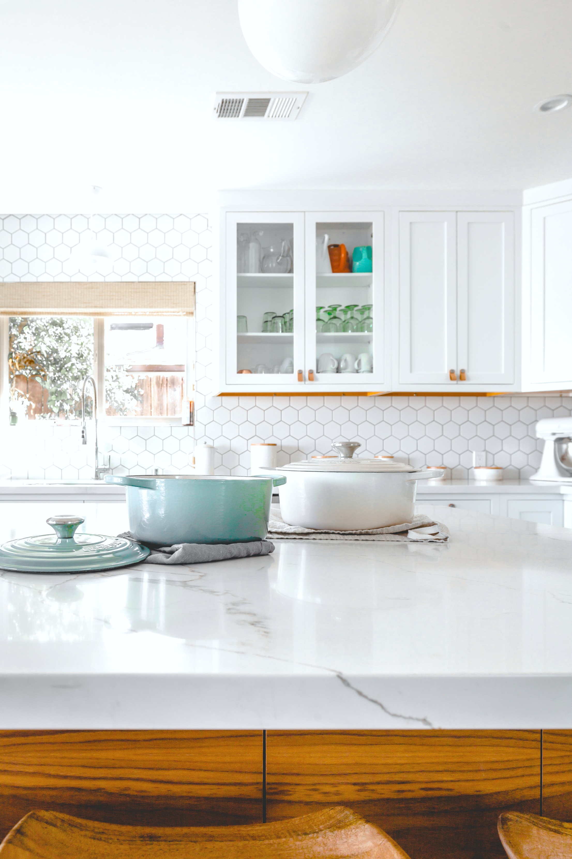 A close up of cooking pots to be used for cooking in a beautiful white kitchen with many appliances. 