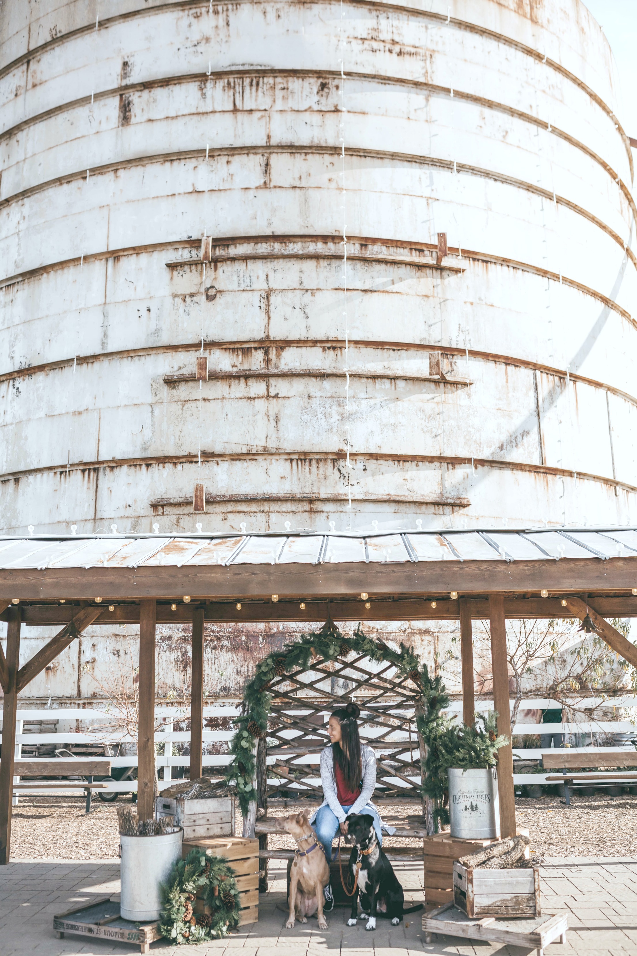 A silo is behind a woman selling wreaths and other greenery. Steel buildings on a rural property.