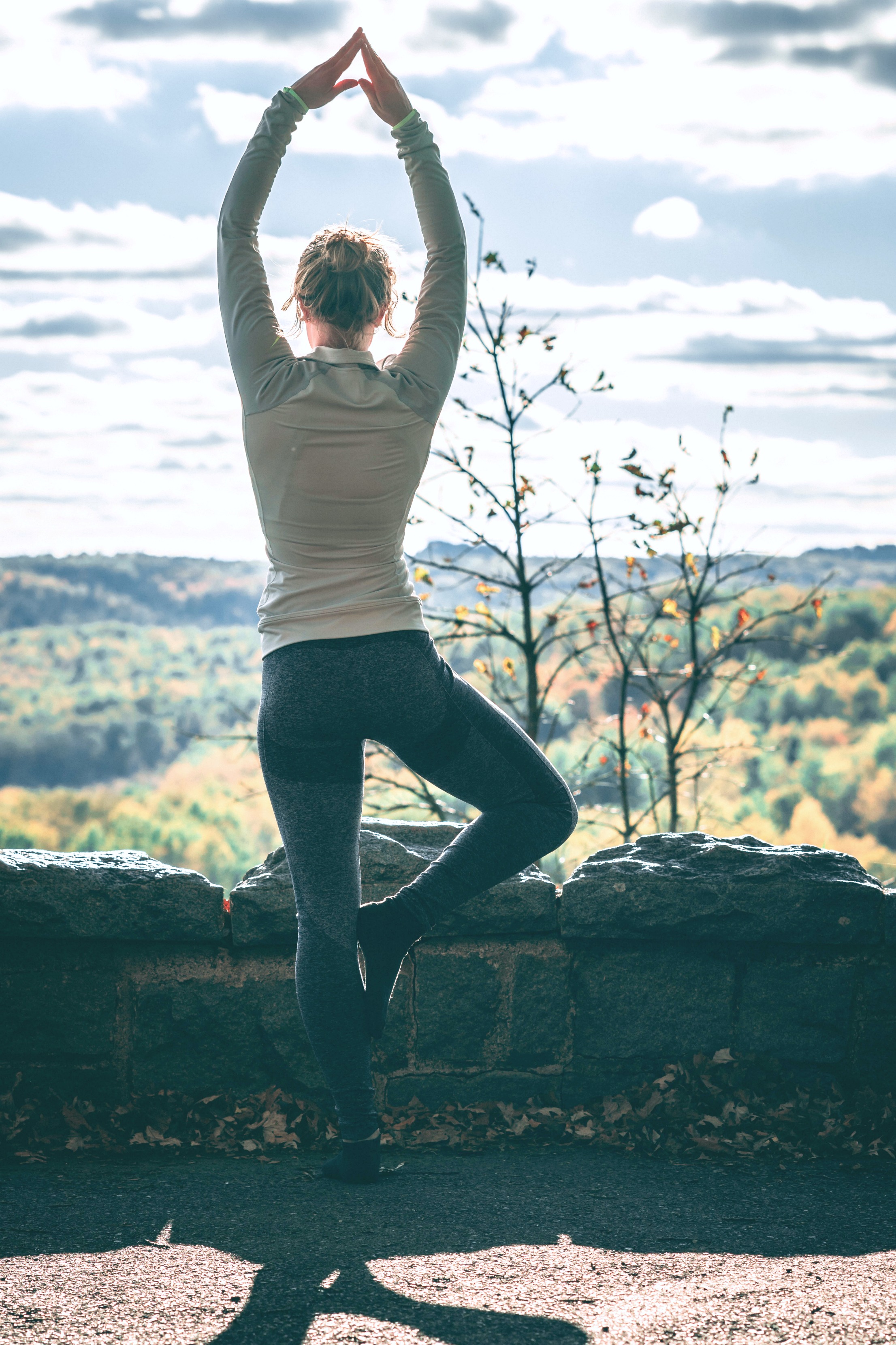 Woman stands at a hillside and does yoga, she strikes a pose. One of the wellness boosting exercises.