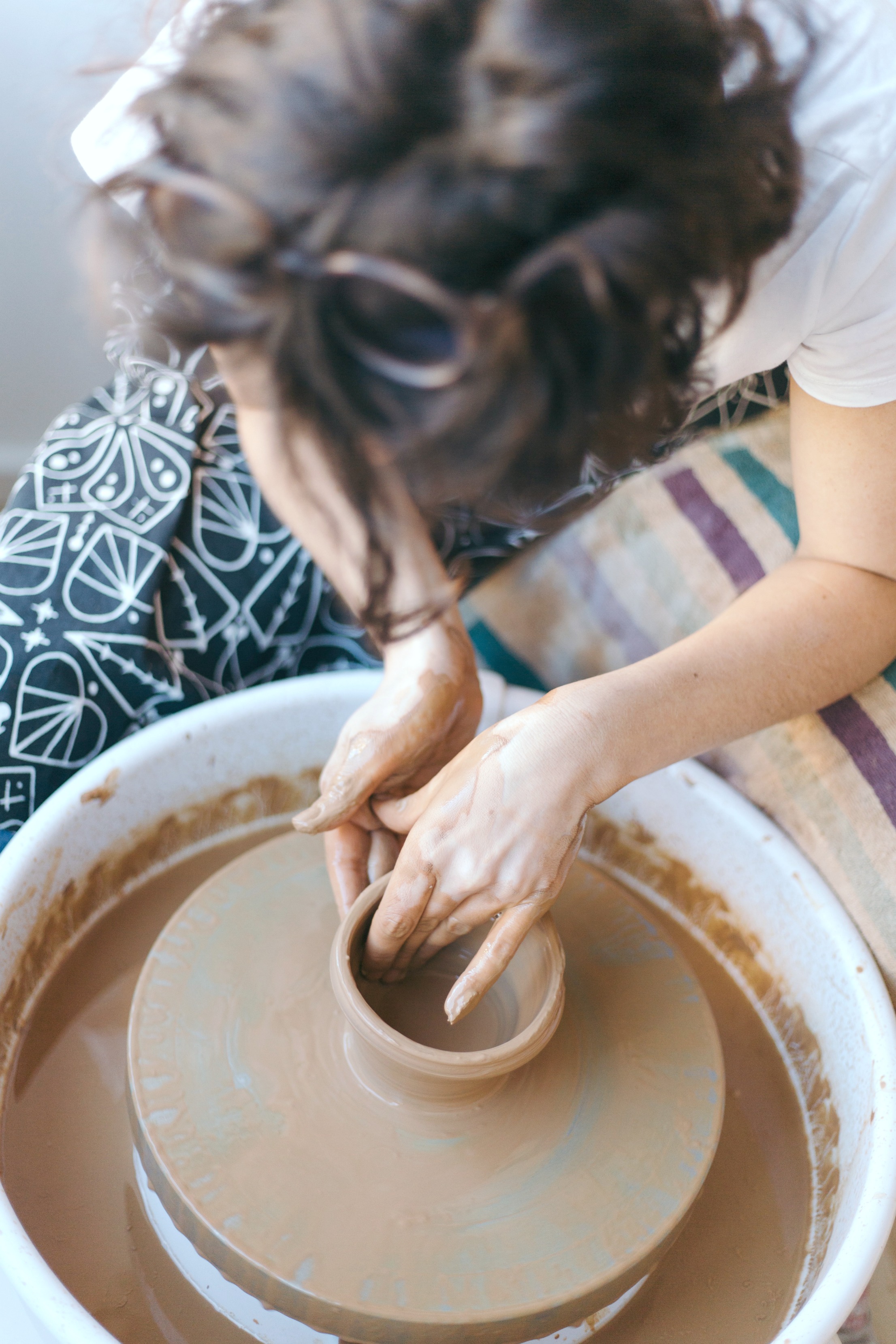 Woman is bending over pottery wheel, enthralled with doing her art. 