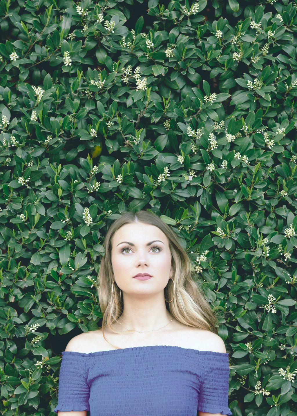 Woman stands in front of a green live plant wall, looks up pensively