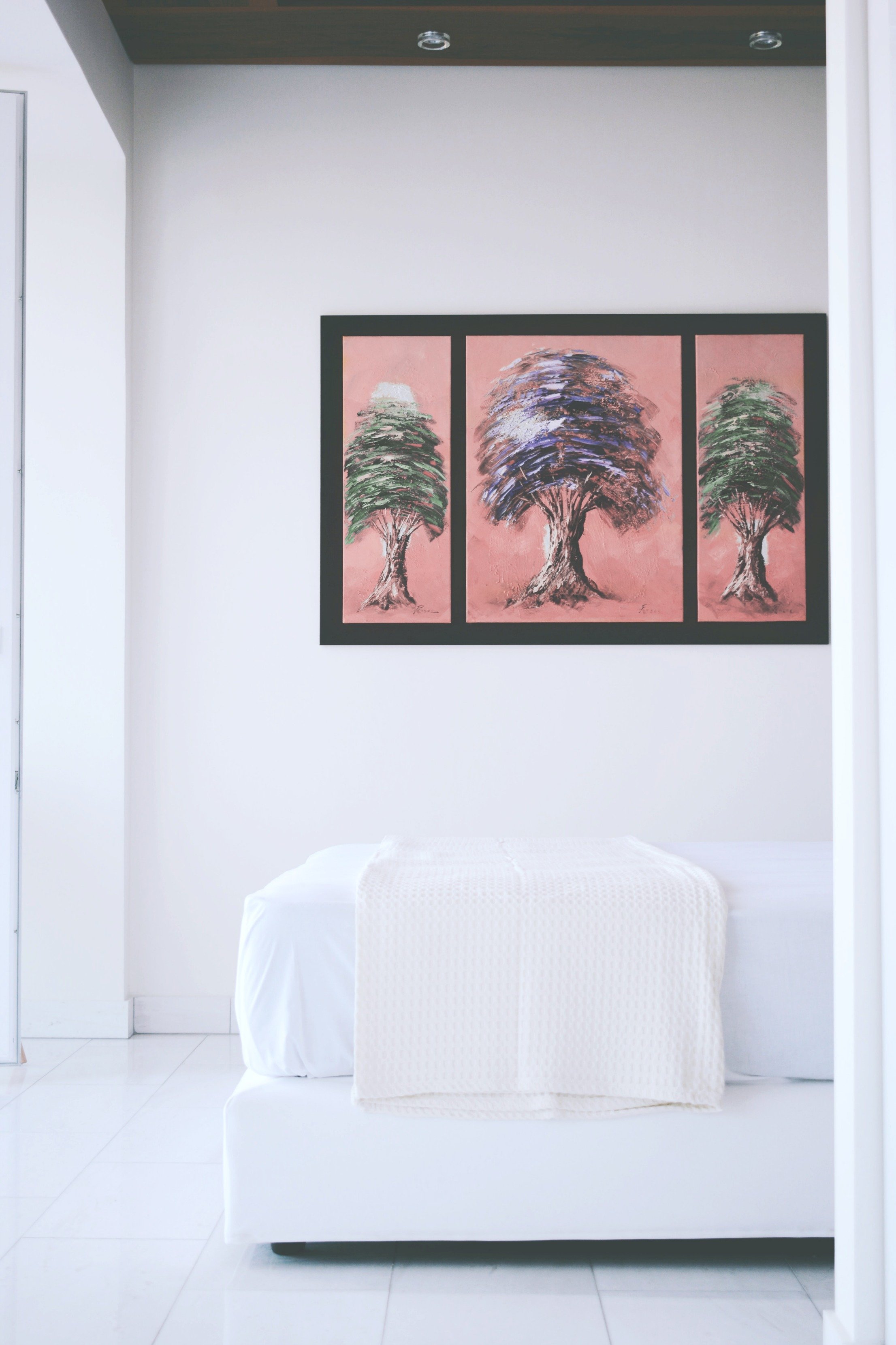 A bedroom that features the end of a mattress and bed, pretty artwork is behind it against a white wall.