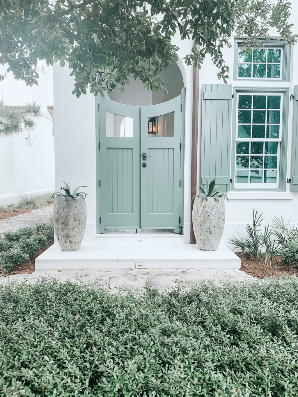 A beautiful white house with a green door, two potted plants are next to the doorway.